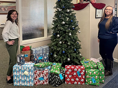 Two Women Next to Large Wrapped Presents Under a Christmas Tree