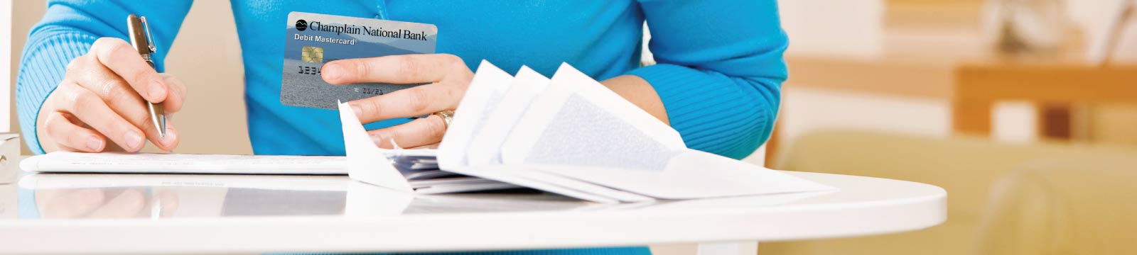 Woman's Hand Holding a Debit Card While Writing Checks