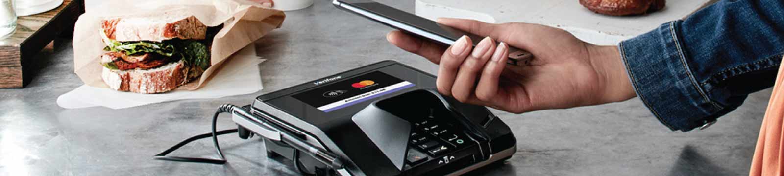 Person Holding a Phone Next to a Point of Sale Terminal