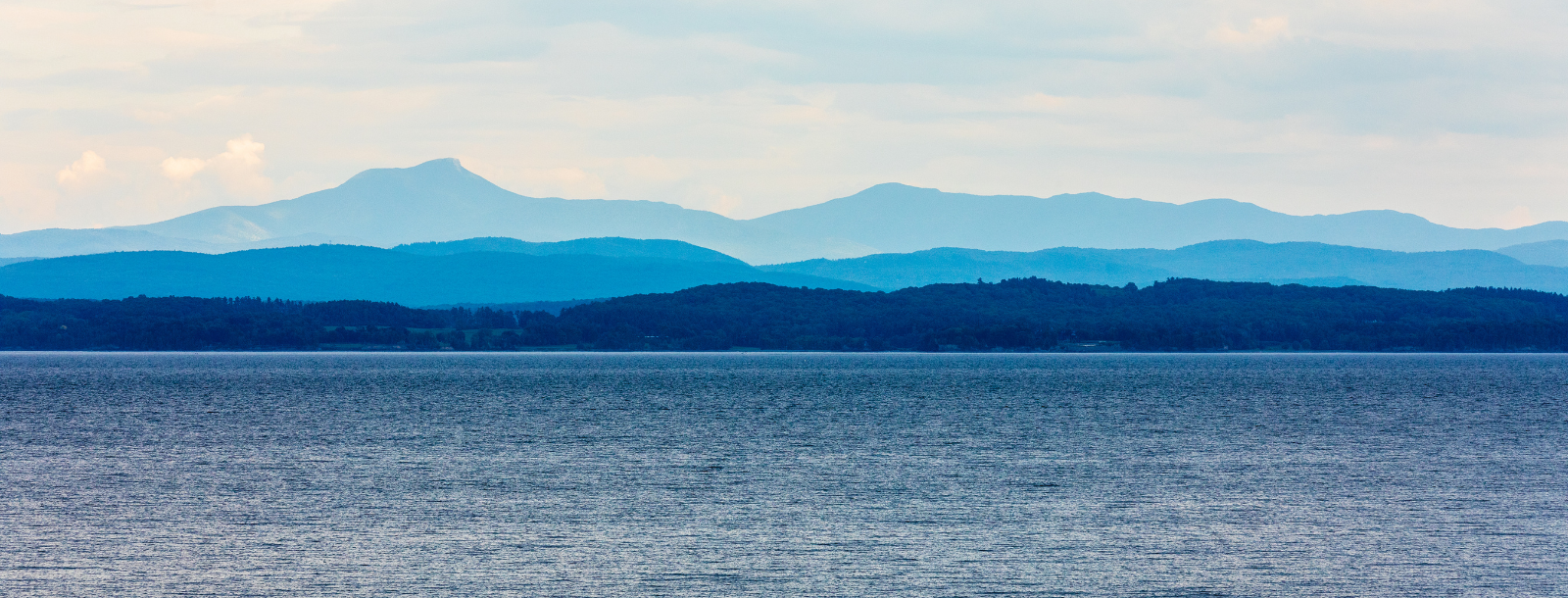 A landscape photo of Lake Champlain with trees and mountains in the background