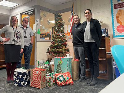 Four People Standing Next to a Christmas Tree with Wrapped Presents Underneath