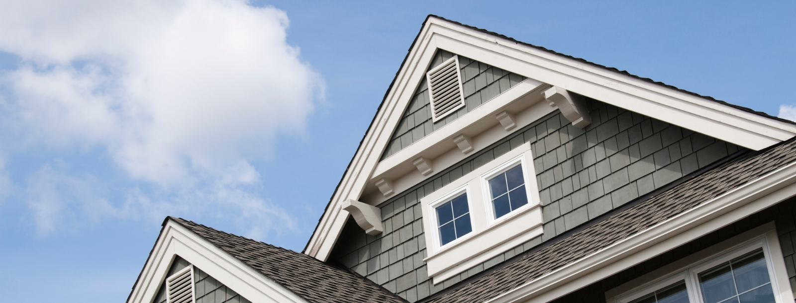 An image of the roof peak of a house with a blue sky behind it