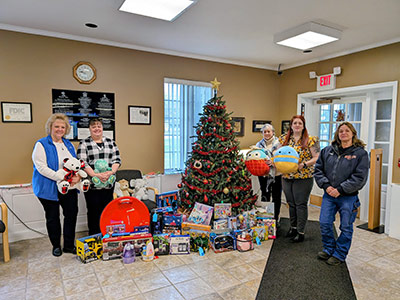 Five People Holding Toys Next to a Christmas Tree with Lots of Toys Underneath