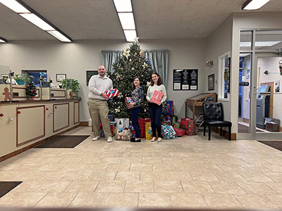 Three People Holding Wrapped Gifts in Front of a Christmas Tree